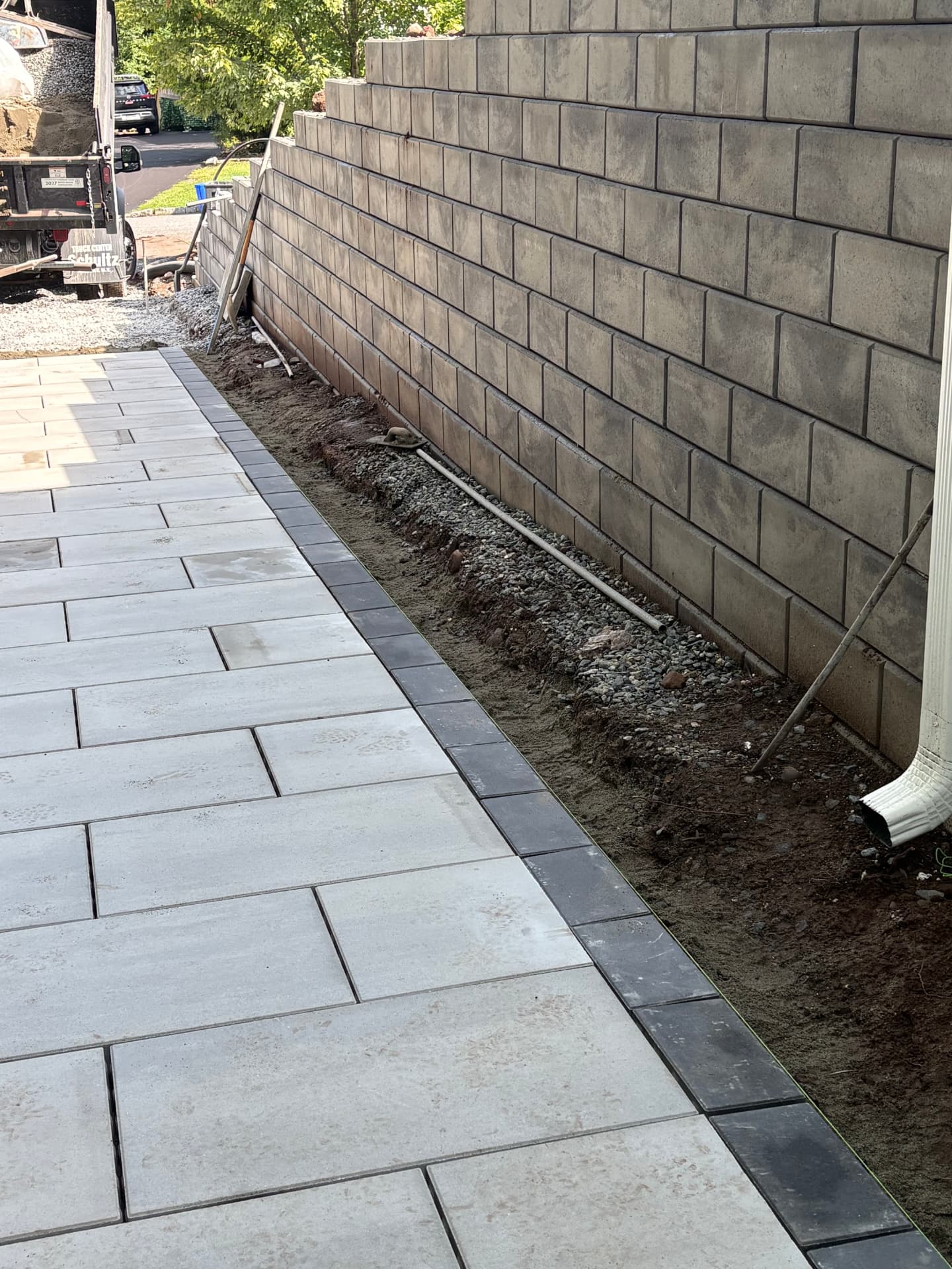 Paver walkway with charcoal border running alongside a block retaining wall