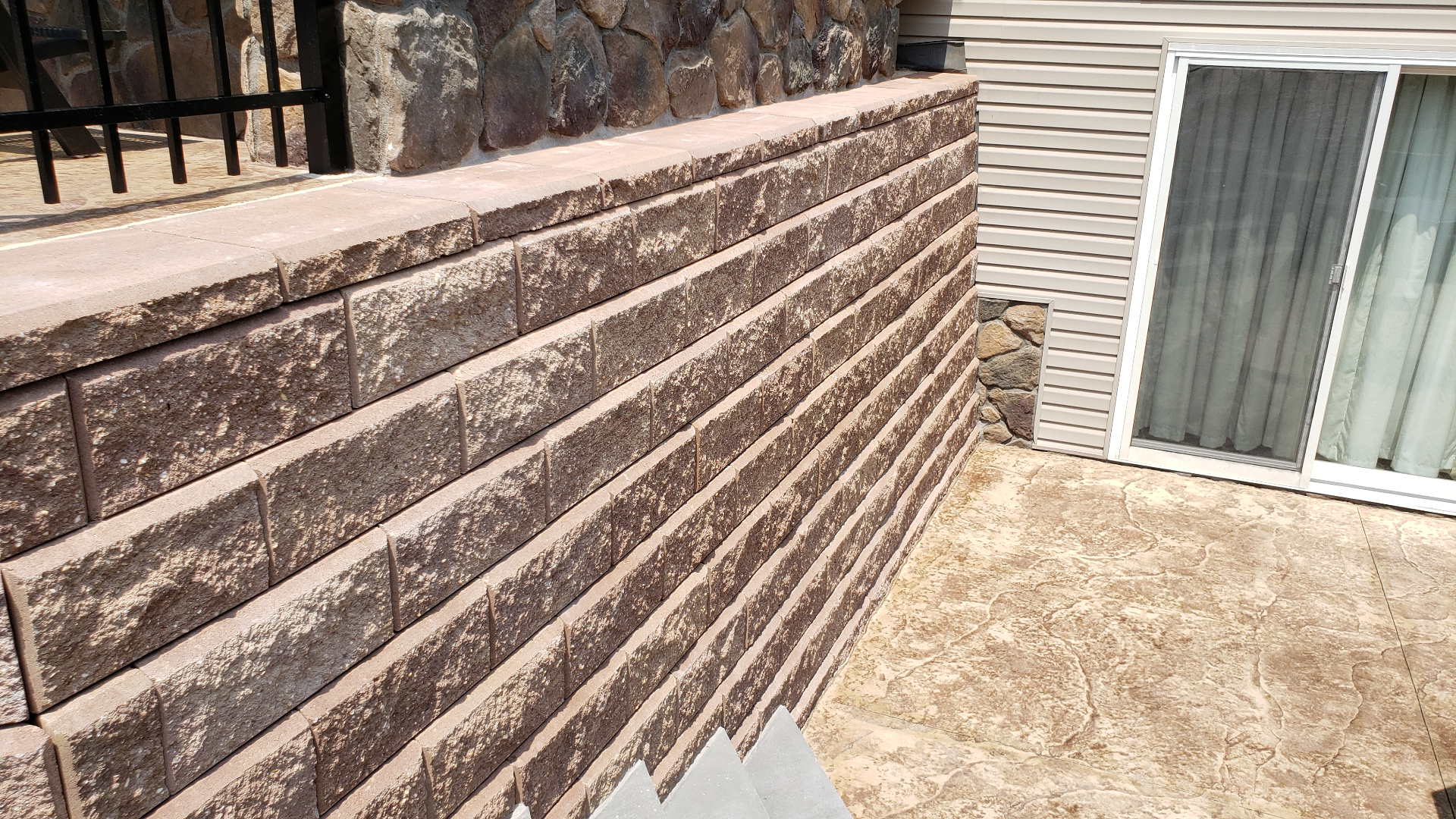 Brown segmental block retaining wall beside stamped patio